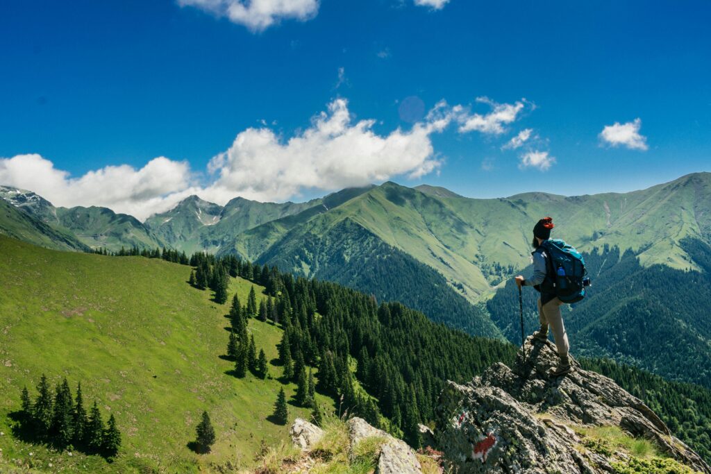 pexels-photo-1271619-1271619 Adventurous hiker enjoying breathtaking views of lush green mountains in Romania under a clear blue sky.